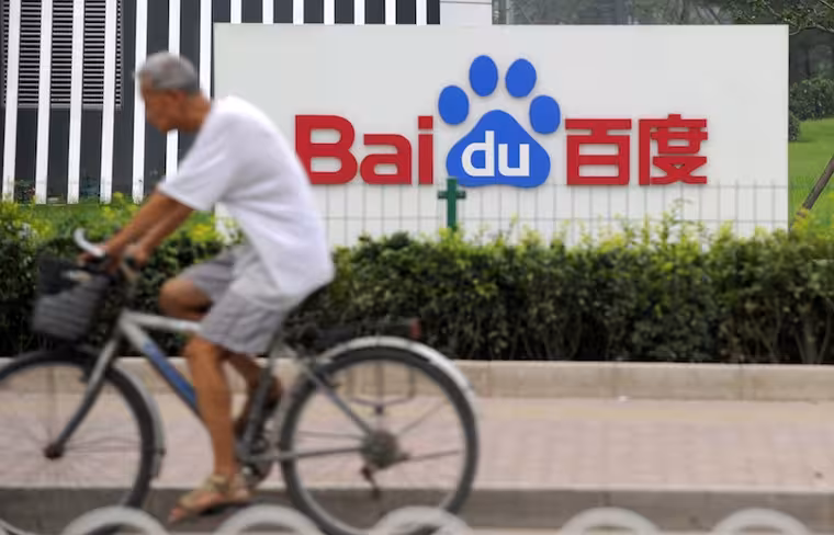 A man rides a bicycle past the logo of B