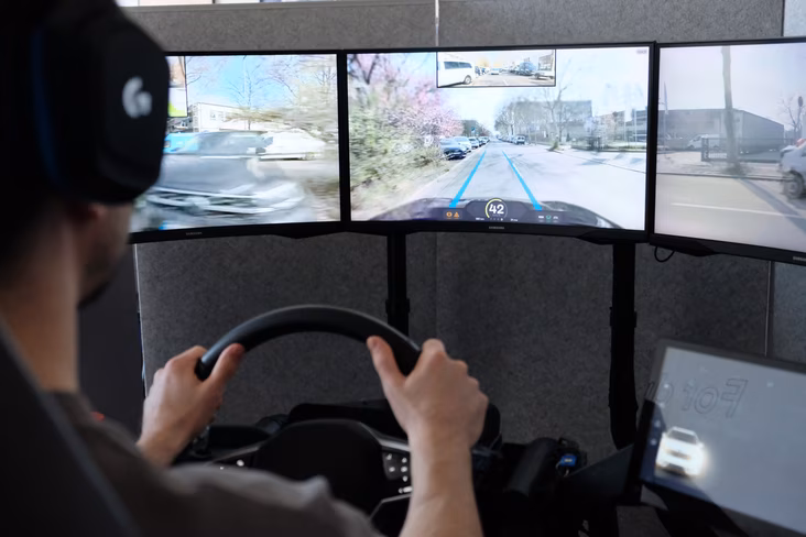 A Vay teledriver holding a steering wheel and watching the car drive on a screen