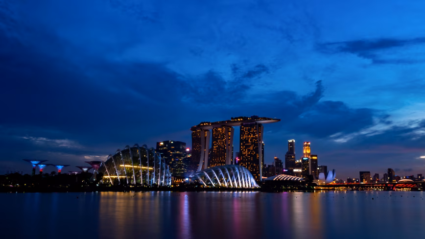 Singapore's Marina Bay skyline at dusk, with Marina Bay Sands, Gardens by the Bay and the Singapore Flyer lit up above the water.