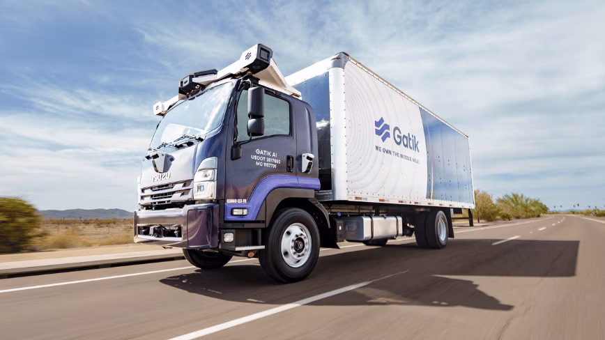 An autonomous Gatik delivery truck driving on a multi-lane highway, equipped with roof sensors and branded with the Gatik logo
