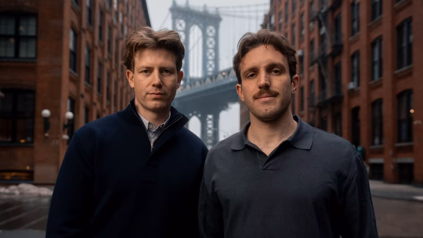 Profound co-founders James Cadwallader and Dylan Babbs, photographed on a Brooklyn street with the Manhattan Bridge behind them.