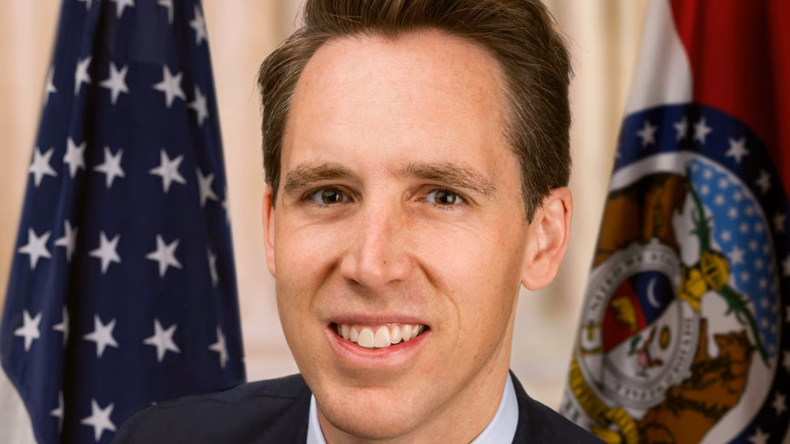 Official Senate portrait of Josh Hawley in a dark suit, photographed between the US and Missouri flags.
