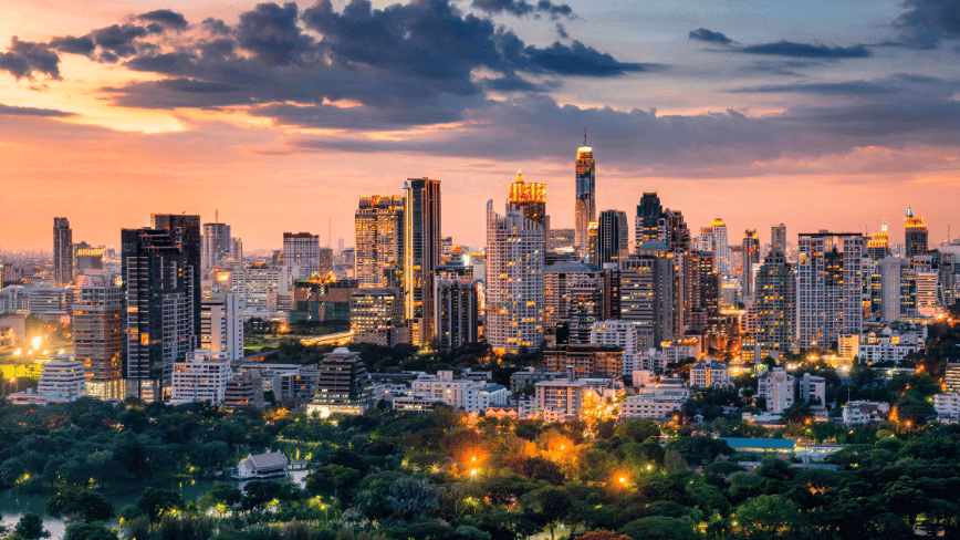 The Bangkok skyline at dusk, with high-rise towers and parkland below