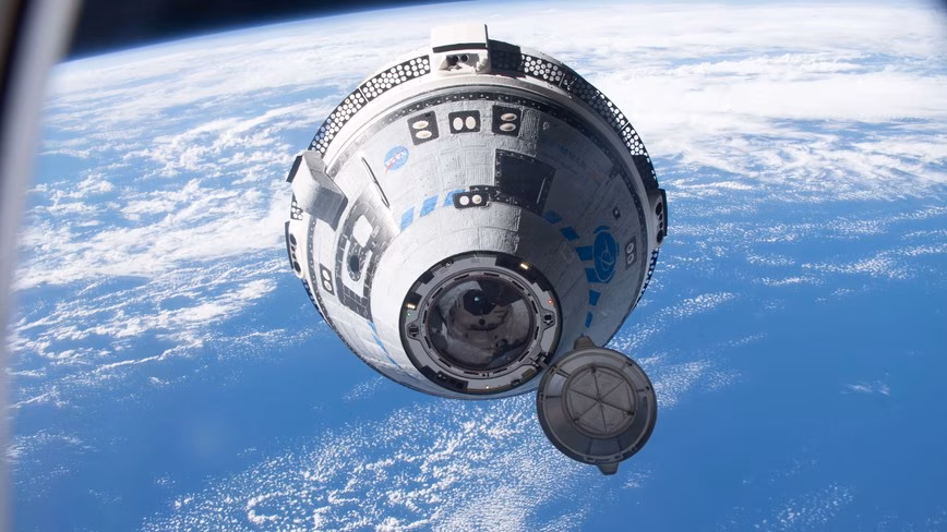 Boeing's Starliner capsule in orbit, its docking hatch cover open, with the Earth's clouds and ocean below