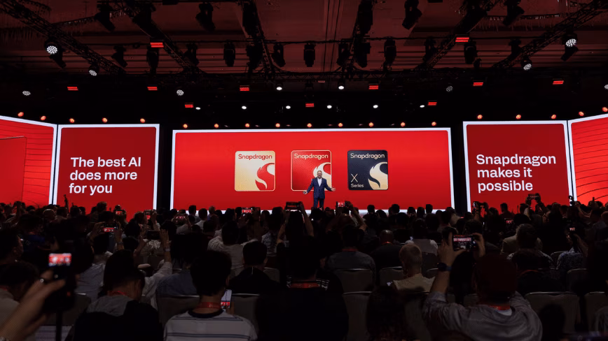 Cristiano Amon on stage in front of a large red screen showing three Snapdragon chip badges, with the audience in the foreground