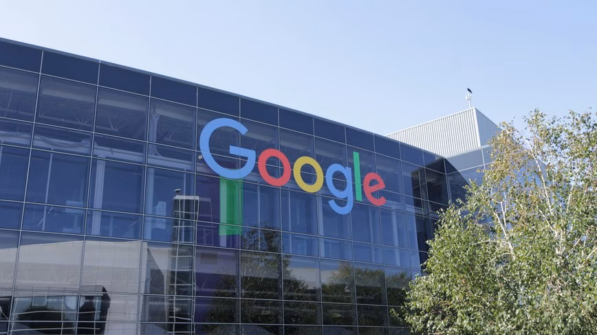 Google's colourful logo on the glass facade of the company's headquarters building, with a birch tree in front
