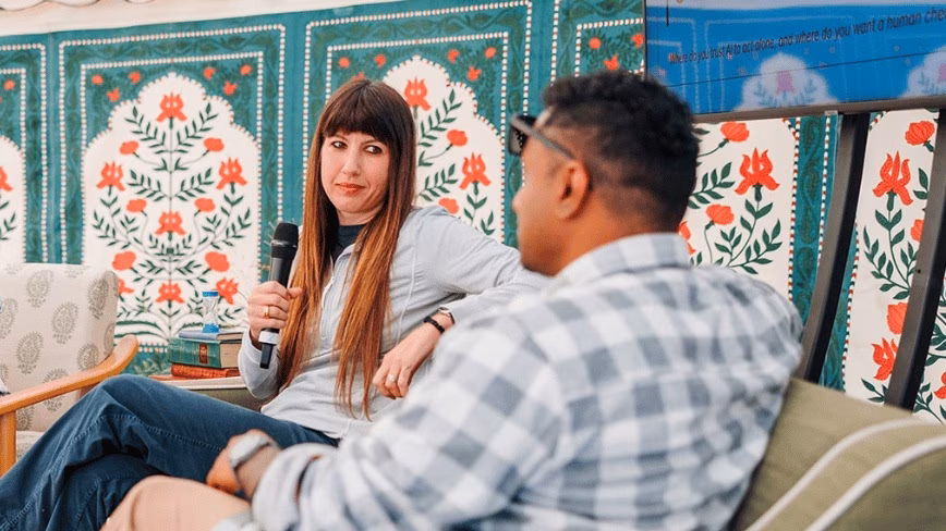 Grady Sokaras of Zapier holding a microphone on a sofa, facing a man in a checked shirt, in front of a green and red floral wall