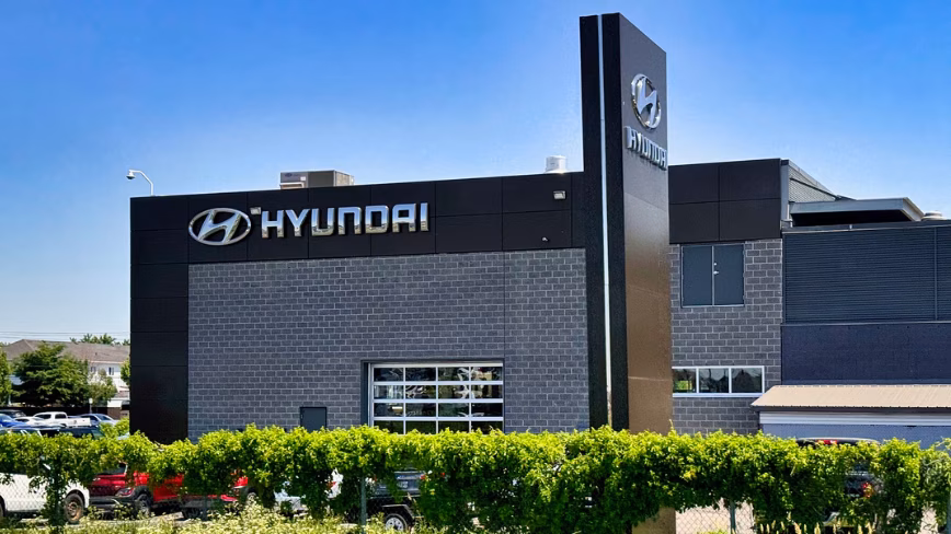 A Hyundai car dealership with illuminated signage and a tall pylon sign, under a clear blue sky.