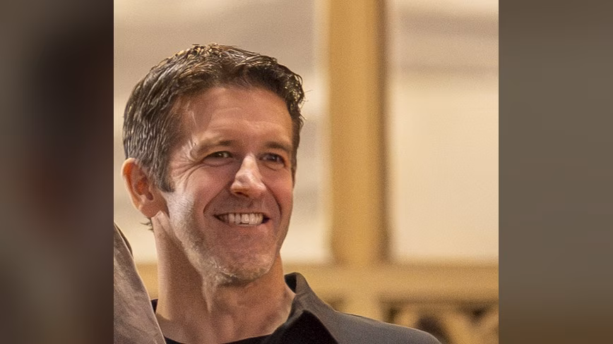 John Ternus, in a dark button-up shirt, smiles at an Apple event