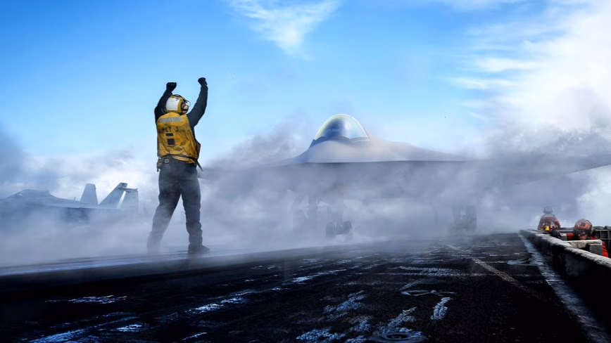 Artist's rendering of a tailless stealth fighter on a misty aircraft carrier deck as a flight director in a yellow vest signals