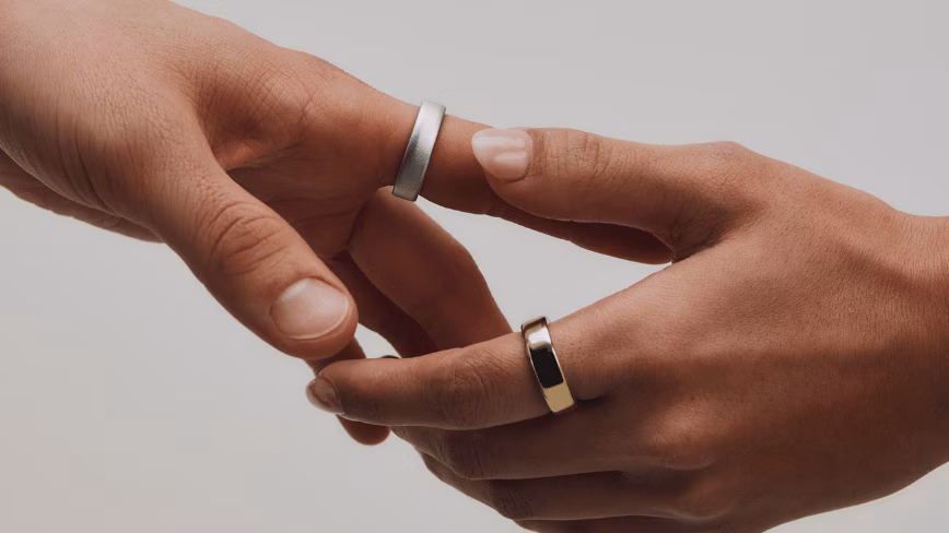 Two hands, one wearing a silver Oura Ring 5 and the other a gold Oura Ring 5.