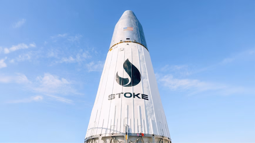 White rocket upper stage with a metallic nose cone and the Stoke logo, standing against a clear blue sky