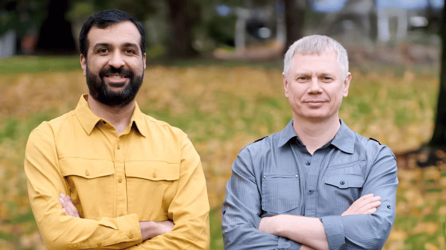 Temporal co-founders Samar Abbas, in a mustard shirt, and Maxim Fateev, in a grey shirt, standing with arms crossed in a park with autumn leaves