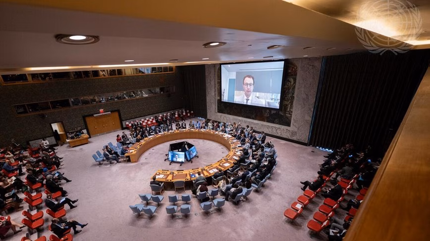Dario Amodei appears on a large video screen above the UN Security Council chamber as delegates sit at the horseshoe table.