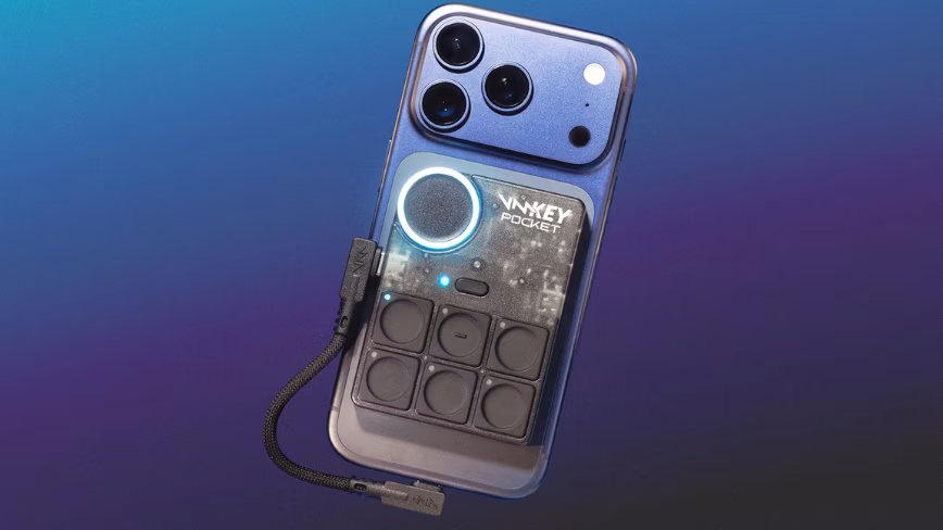 The Voicemod Key Pocket, a small black control pad with six buttons and a lit dial, attached to the back of a blue phone.