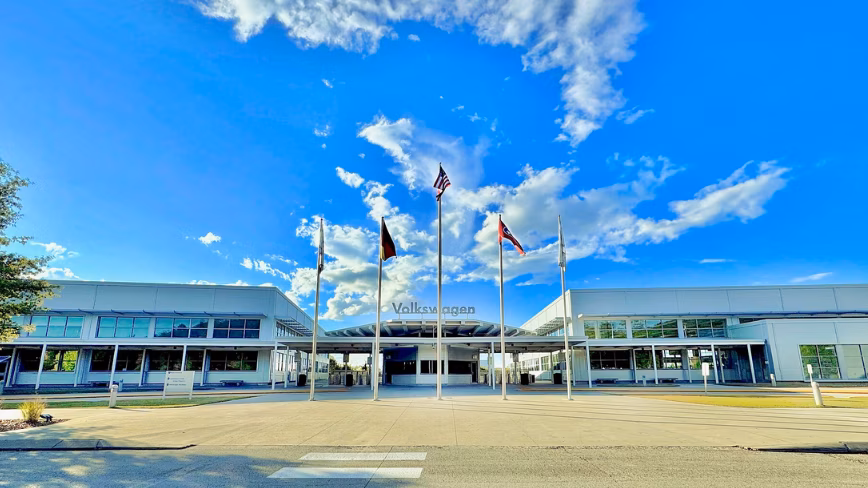 Flags fly outside the entrance to the Volkswagen assembly plant in Chattanooga, Tennessee, under a blue sky.
