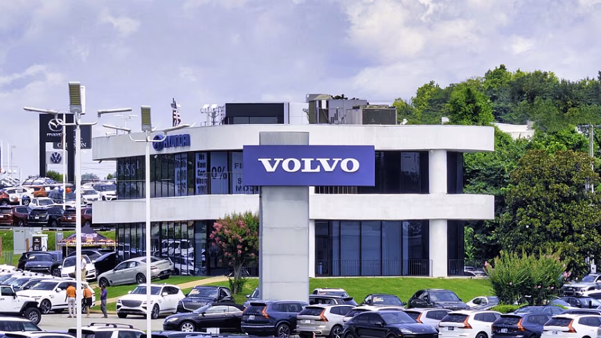 A Volvo dealership with a large VOLVO sign above a forecourt filled with parked cars.