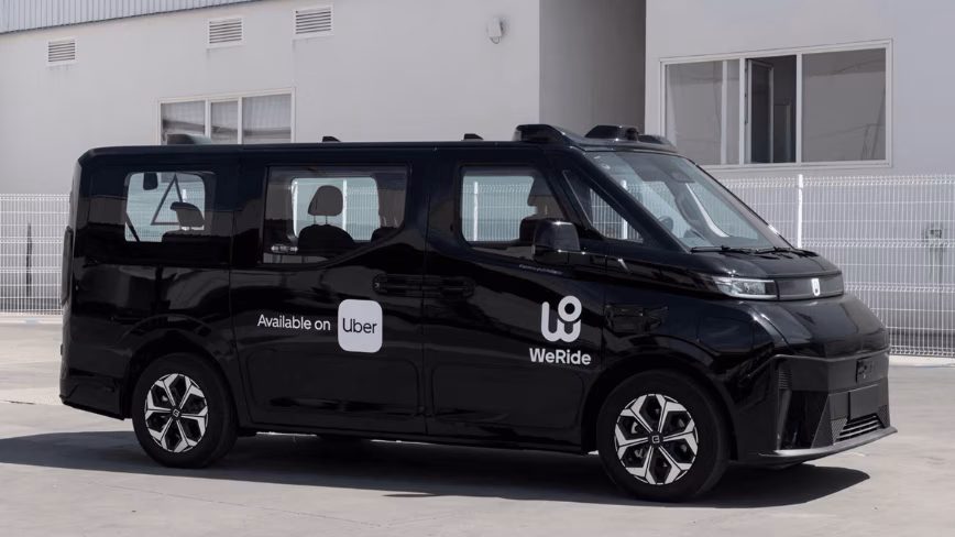 Black WeRide GXR autonomous van with roof-mounted sensors and "Available on Uber" branding, parked in front of a white industrial building
