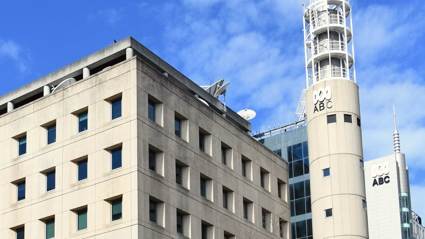 ABC logos on a cylindrical tower and a neighbouring building beside a stone office block with rooftop satellite dishes.