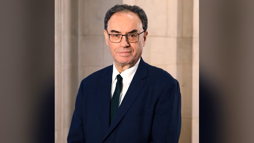 Bank of England governor Andrew Bailey in glasses, a navy suit and dark green tie, standing against a pale stone wall