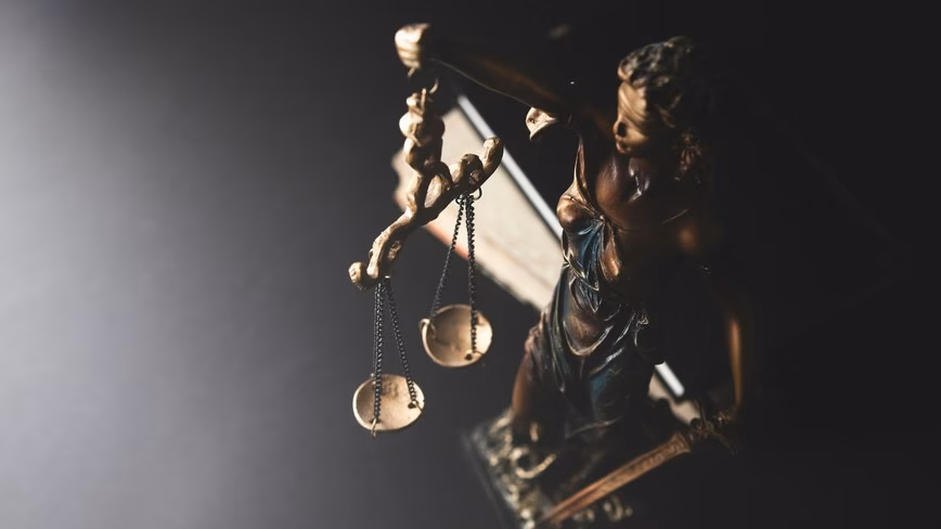 A bronze statue of blindfolded Lady Justice holding the scales of justice, seen from above against a dark background