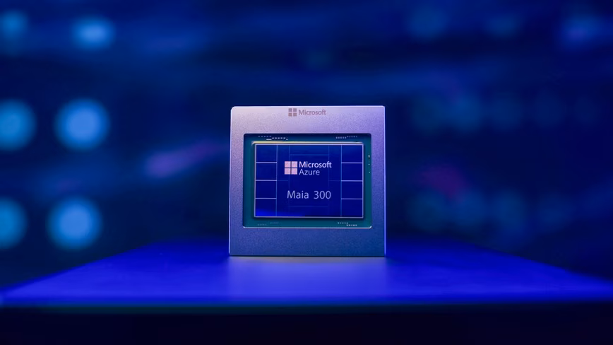 Microsoft Azure Maia 300 AI chip, a square silver package with a blue die, lit in blue on a dark reflective surface
