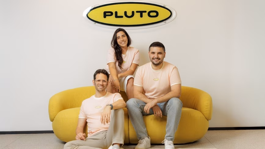 Pluto Security co-founders Tal Ofer Regev, Shahar Bahat and Gil Maman, in matching peach T-shirts, on and beside a yellow sofa below a yellow Pluto sign