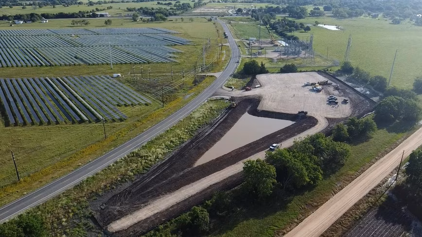 An aerial view of a solar array beside a road, with earthmoving machinery working on a cleared site.